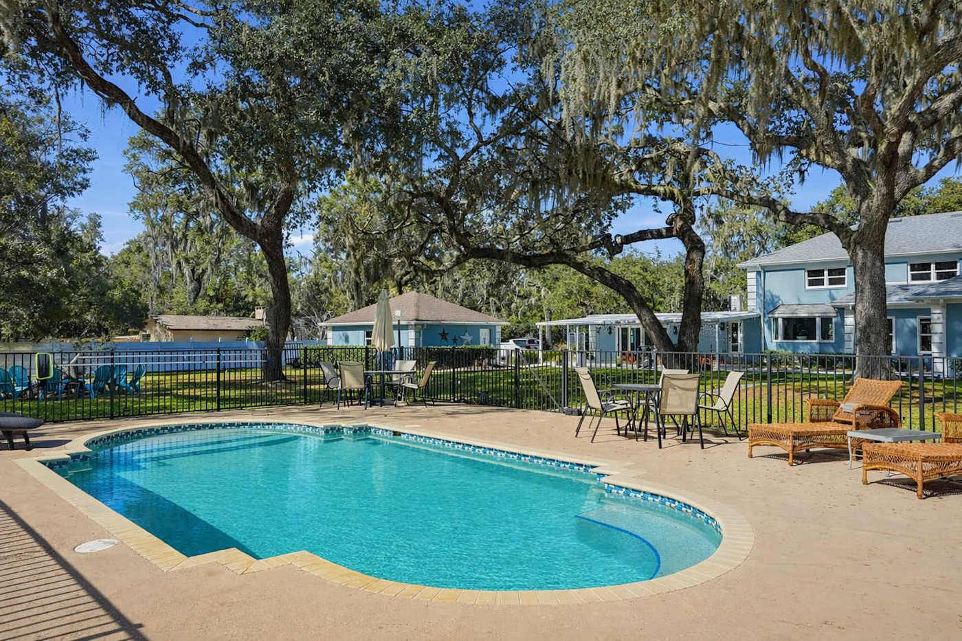 The estate pool and sun deck under the live oaks, with the house, covered patio, and lake beyond the fence